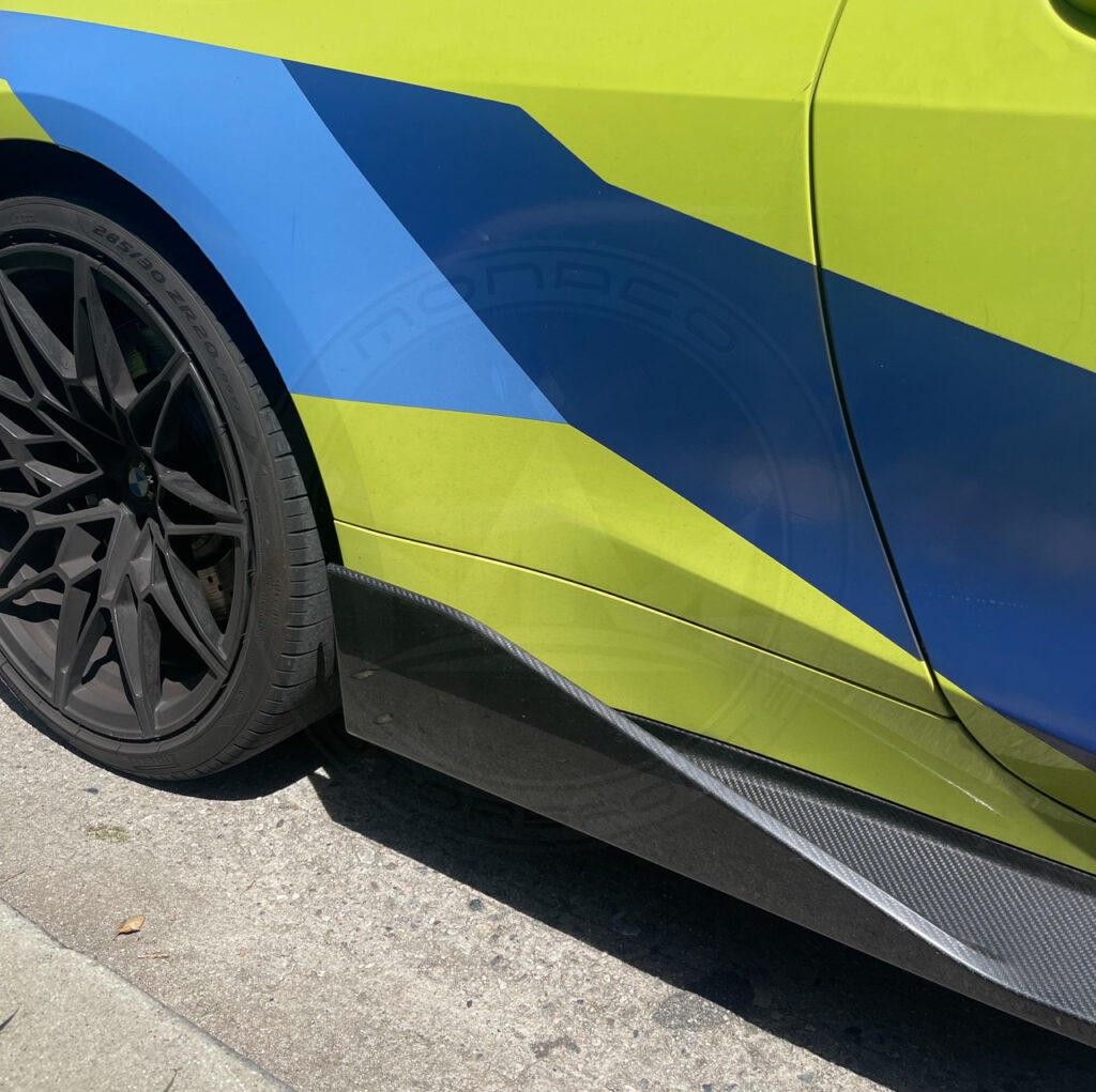 Close-up of a car's side with blue and yellow paint and black wheel.