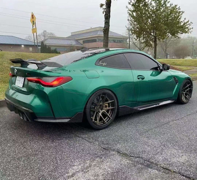 Green sports car parked on wet pavement near trees and industrial buildings.