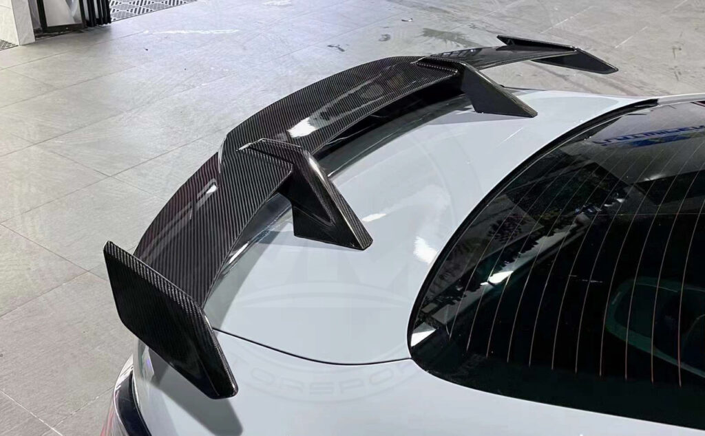 Close-up of a carbon fiber car spoiler on a white vehicle.