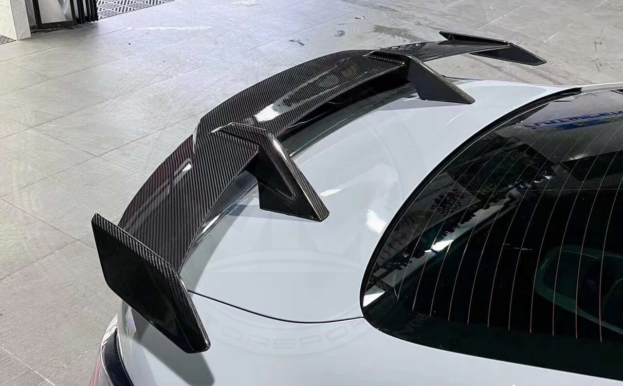 Close-up of a carbon fiber car spoiler on a white vehicle.